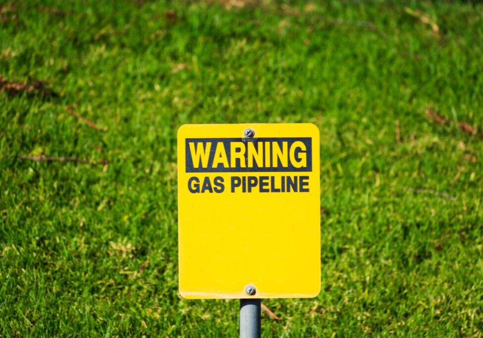 Warning gas pipeline sign with blurred background of green landscape.